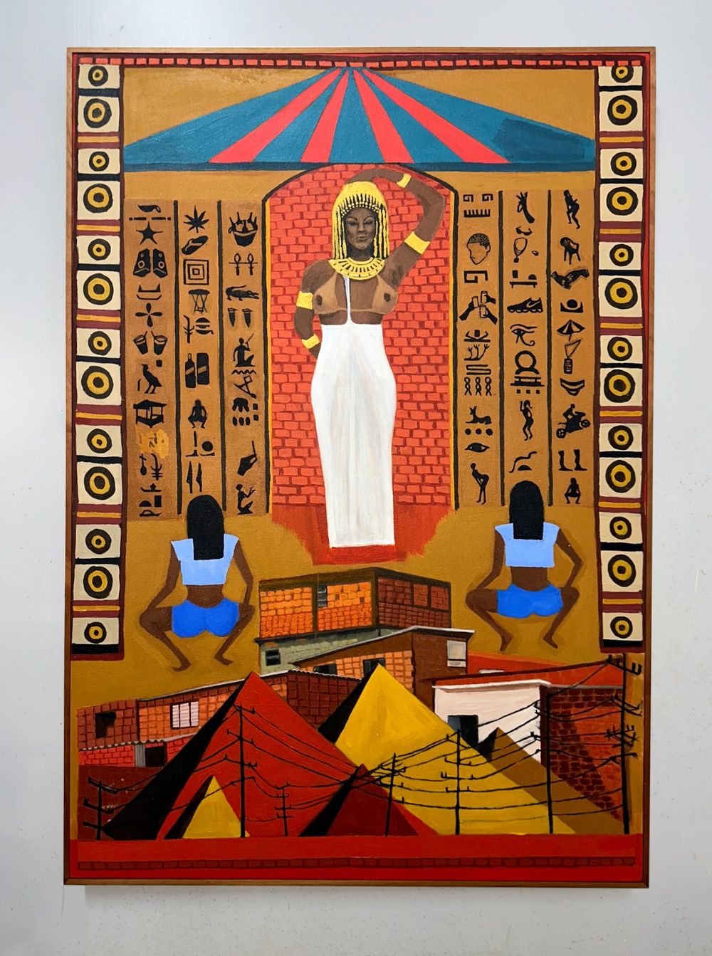 Pintura vertical com mulher de adereço egípcio dourado sob um arco de tijolos, entre colunas de pictogramas, dançarinas de costas e pirâmides sobre casas de favela.