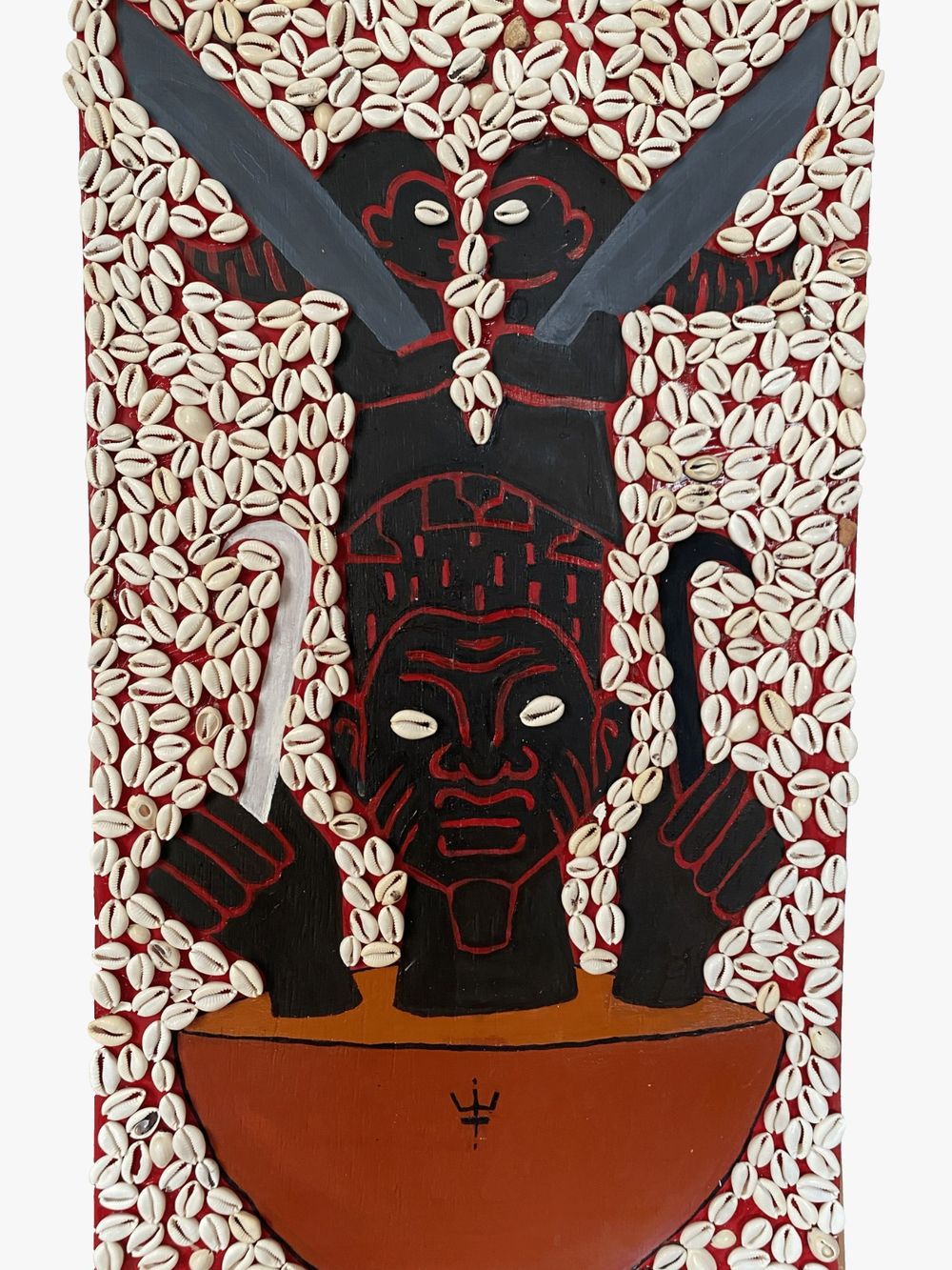 Painel vertical coberto de búzios, com rosto negro de olhos de búzio, lâminas cruzadas e vasilha vermelha com símbolo de tridente.